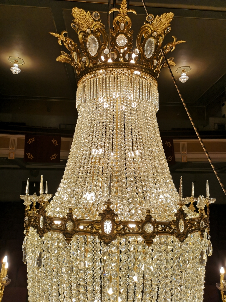 Remat de la làmpara amb una gran corona de bronze amb decoració de fulles i espills que tenen incrustracions de cristalls a mode de pedres precioses (foto Iratxo Atzi). Remat de la làmpara amb una gran corona de bronze amb decoració de fulles i espills que tenen incrustracions de cristalls a mode de pedres precioses (foto Iratxo Atzi).